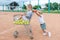 Little sister rolls shopping trolley with the brother on tennis court