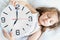 Little sleeping girl with big, huge clock in hands. Early morning wake up before kindergaten,school. White pillow, blanket in bed