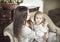 A little sleepy baby sits on her motherâ€™s lap. Mom combs her daughterâ€™s hair.