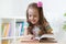 Little smart girl looking at book while sitting on chair in nursery