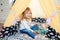 Little smiling blonde 3 years old girl play in yellow tent wigwam in her bedroom. Time to play during self isolation on quarantine