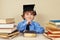 Little smiling boy in academic hat among old books