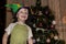 A little smiling boy wearing harlequin hat standing on background of New Year tree.