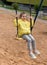 A little smiling girl enjoying swinging in a playground of an apartment house`s court yard