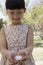 Little smiling girl looking down at a cherry blossom in her cupped hands in a park in springtime