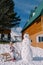 Little smiling girl sits on a sled near a snowman near a wooden chalet