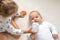 Little smiling kids playing together on bed. Sibling preschool sister give water from bottle to newborn, take care of