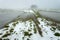 Little snow and frozen water in a farmland, view on a foggy January day