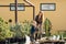 Little son helps mom to water the pots of plants in garden center.