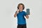 Little sportive boy child in headphones smiling at camera, showing thumbs up, holding smartphone with blank screen while
