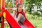 Little sportive girl playing on playground, sitting on the slide