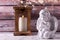 Little statue of white angle and lantern with burning candle  against brown textured wall.