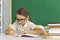 Little student girl sitting at desk in classroom and writing in her school notebook