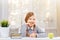 Little student girl sitting at the table. Schoolgirl with a pen in hand and a notebook. The child smiles thoughtfully.