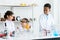 Little student group in white lab coat with many laboratory tools on shelves and table in chemistry classroom. A little girl with