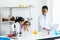 Little student group in white lab coat with many laboratory tools on shelves and table in chemistry classroom. A little girl