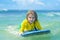 Little surfer learn to ride on surfboard on sea wave. Summer vacation with child. Kid girl is learning surfing, riding a