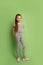 Little teenager girl in gray jeans and gray blouse stands on green background in studio. Copy space