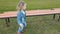 a little three-year-old girl in denim clothes walking in the Park on the green grass near the bench.