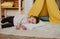 a little tired girl lies on the floor with her head on a pillow, next to a yellow teepee