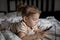 Little toddle girl playing with smartphone laying on the bed at home. Caucasian toddler girl.