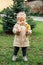 Little toddler baby girl in trench coat picking yellow dandelions in spring garden. Cute baby girl enjoying the simple