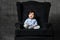 Little toddler in blue shirt, gray pants, white booties. Screaming, sitting in black armchair on gray studio background. Close up