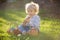 Little toddler boy, eating chocolate bunny in garden on sunset, easter eggs