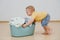 Little toddler boy is moving heavy laundry basin full of washed towels