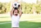 Little toddler boy playing football on soccer field outdoors: the kid is holding ball above head and shouting ready to throw it