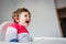 Little toddler boy sitting in a chair for feeding in a room in breakfast time