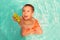 Little toddler boy sitting in swimming pool with funny face expression and shooting or aiming up with green water gun