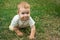 Little toddler boy trains his crawling skills. The child happily crawls on the green grass.