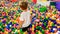 Little toddler boy walking and climbing over lots of colorful plastic ball on the playground at shopping mall