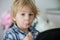 Little toddler child, blond boy, licking lollipop while watching movie on tablet
