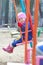 Little toddler girl in dark blue warm overall is sitting on playgrounds swing