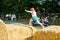 Little toddler girl having fun with running and jumping on hay stack or bale. Funny happy healthy child playing with