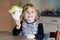 Little toddler girl making craft angel with paper cups, colorful pompoms and glue during pandemic coronavirus quarantine