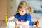 Little toddler girl making craft lantern with paper cups, colorful pompoms and glue during pandemic coronavirus