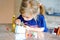 Little toddler girl making craft lantern with paper cups, colorful pompoms and glue during pandemic coronavirus