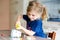 Little toddler girl making craft lantern with paper cups, colorful pompoms and glue during pandemic coronavirus