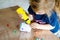 Little toddler girl making craft lantern with paper cups, colorful pompoms and glue during pandemic coronavirus