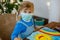 Little toddler girl in medical mask painting rainbow with water colors during pandemic coronavirus quarantine disease