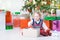 Little toddler girl opening her Christmas present under a beautiful Christmas tree