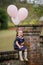 Little toddler girl with pink birthday balloons sitting on a brick wall with a column