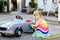 Little toddler girl playing with big vintage toy car and having fun outdoors in summer. Cute child refuel car with water