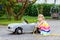 Little toddler girl playing with big vintage toy car and having fun outdoors in summer. Cute child refuel car with water