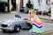 Little toddler girl playing with big vintage toy car and having fun outdoors in summer. Cute child refuel car with water