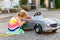 Little toddler girl playing with big vintage toy car and having fun outdoors in summer. Cute child refuel car with water