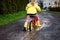 Little toddler girl wearing yellow rain gum boots, running with balance bike during sleet. Happy child driving, biking